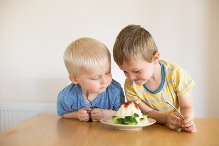2 children eating mashed potato volcanoes with broccoli